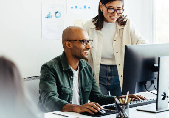 Web developers using a computer together in a creative office. Two business people working on a new software developing project in an office.