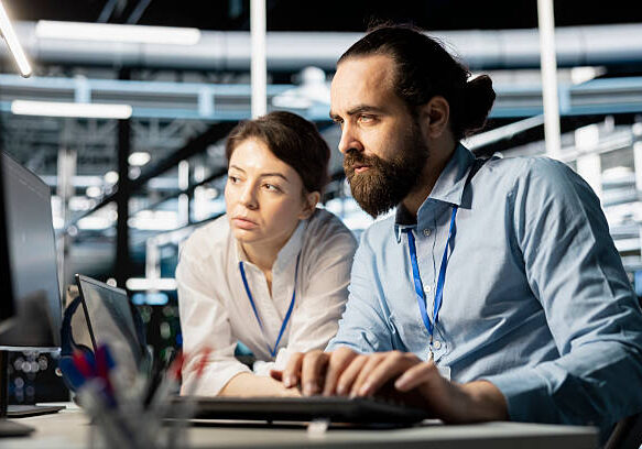 Data center coworkers doing brainstorming, running diagnostic scripts on computer, examining hardware. Server room employees talking, working together to evaluate performance metrics
