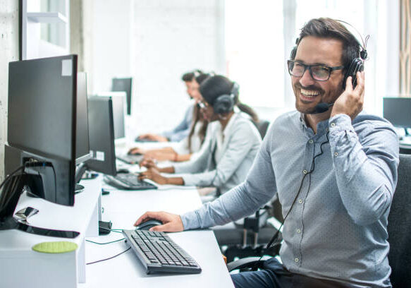 Smiling handsome customer support operator with headset working in call center.